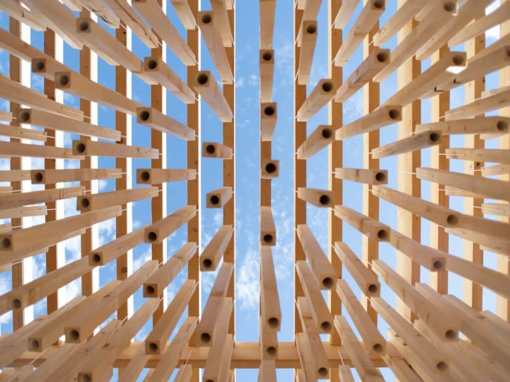 Low angle shot looking up through the hollow wooden slats of Cappella del Suono towards the blue sky.