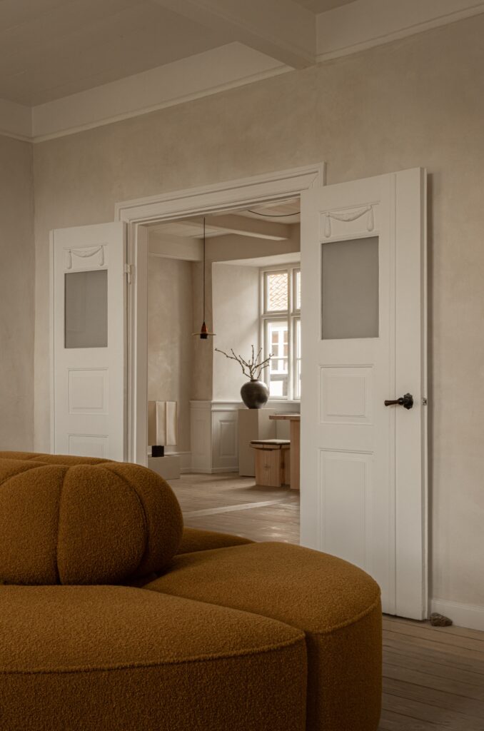 A close-up of a textured ochre-colored curved sofa in a minimalist room featuring classic white double doors and natural light.