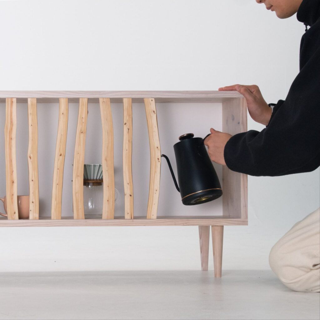 A person interacting with the Hayashi Cabinet, reaching inside a gap between sliding wooden branches.