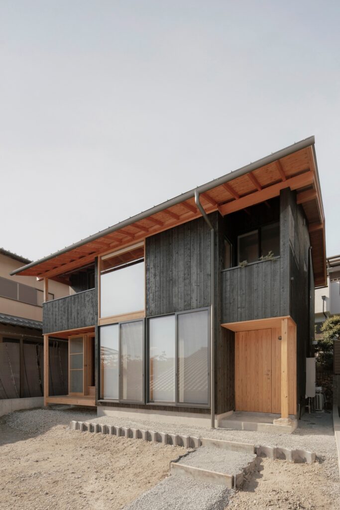 Exterior of a two-story house with black charred cedar (Yakisugi) cladding and large glass windows.