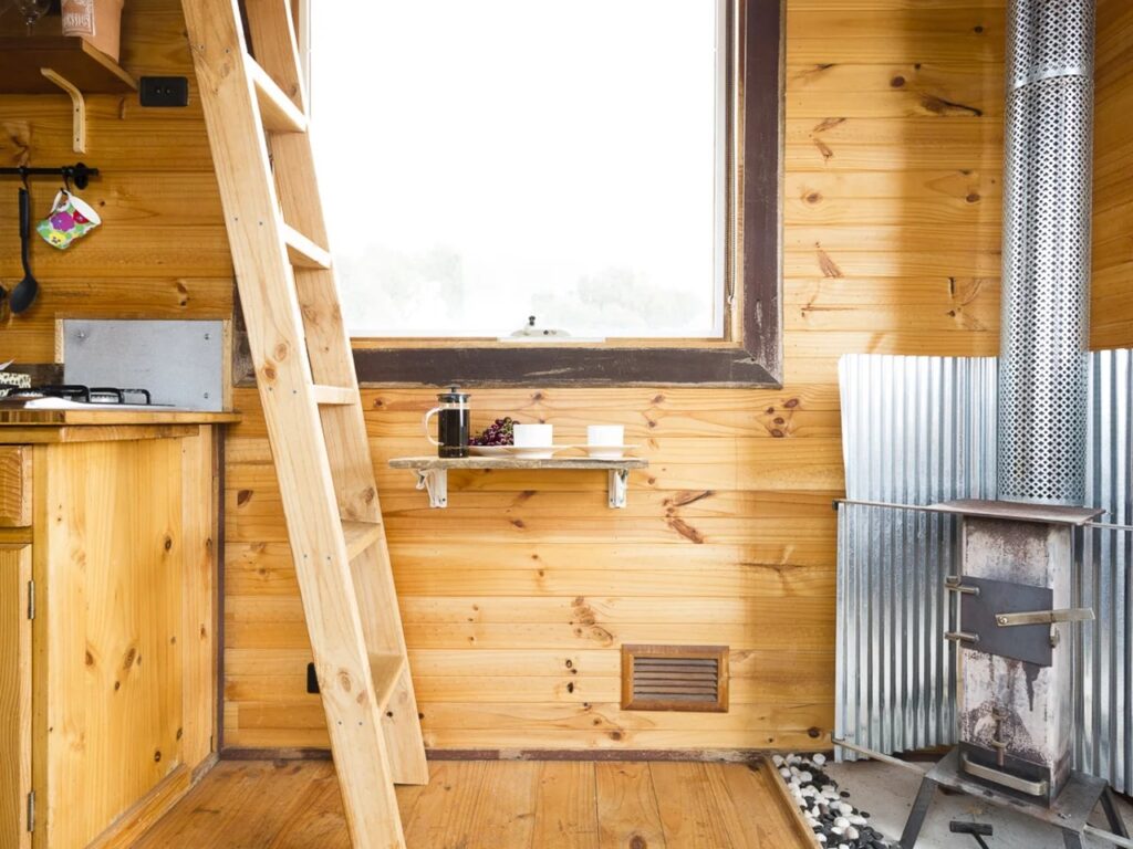 Interior detail of Tallarook Tiny House showing a wooden ladder leading to a loft and a small breakfast nook by the window.