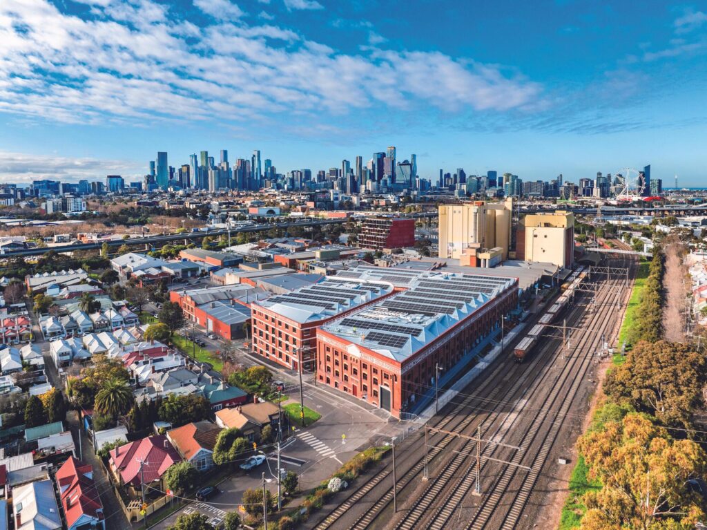 Aerial view of the Younghusband complex showing an extensive 330kW solar panel array on sawtooth roofs with the Melbourne city skyline in the background.