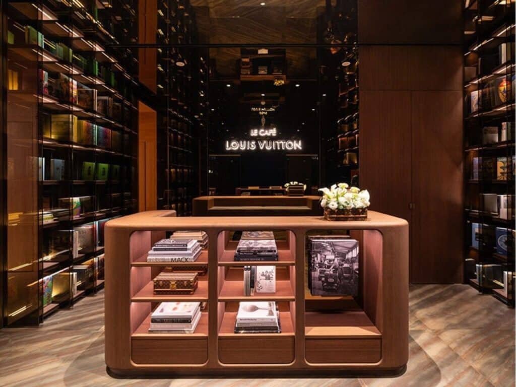 Entry area of Le Caf&eacute; Louis Vuitton in Beijing, featuring mirrored walls, a sleek reception desk, and illuminated bookshelves.