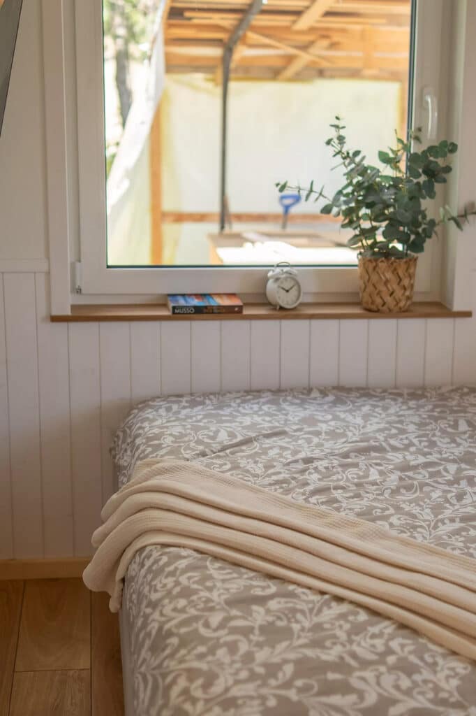 Cozy bedroom interior with a large window, white shiplap walls, and a patterned bedspread.