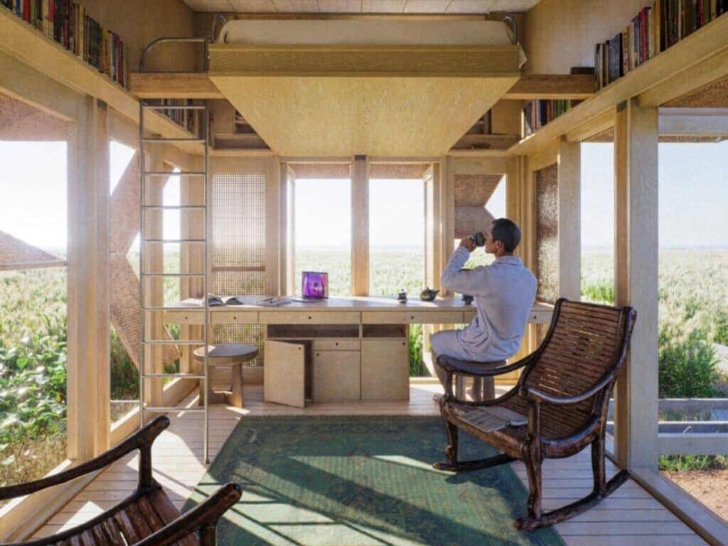Open plan living area of a micro-home with a lofted sleeping area and large windows facing a rural landscape.