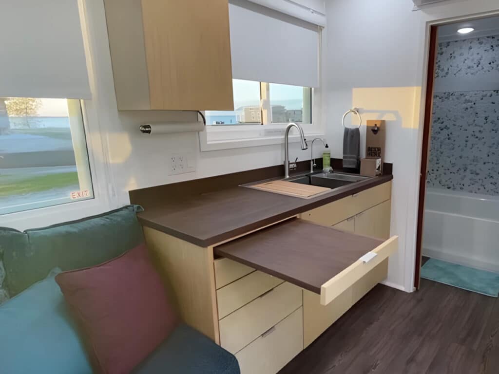 Compact kitchen in the IndigoGo! home featuring a pull-out wooden dining table and sleek cabinetry.