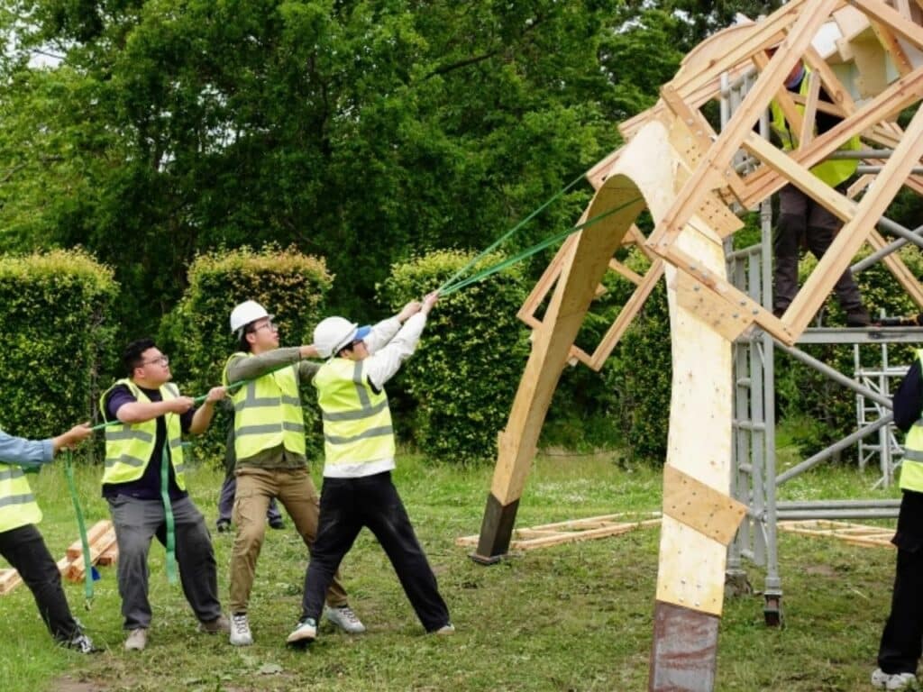 Group of students using tension straps to align a wooden arch of the Arkhive pavilion.