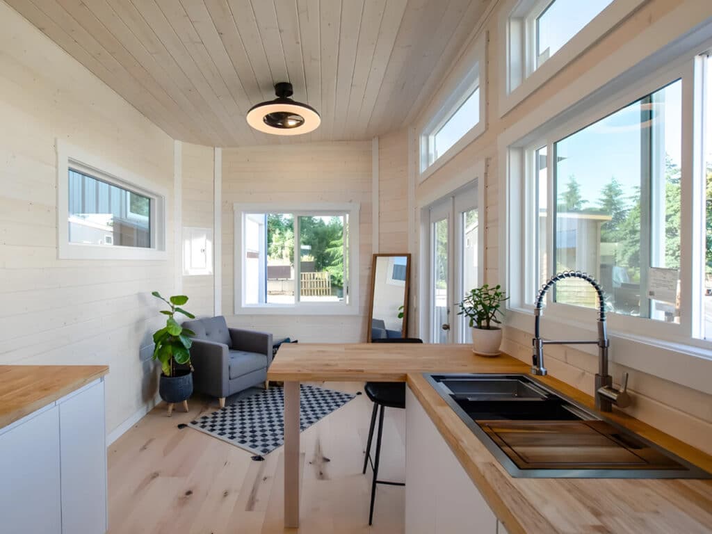 Interior view of the Dove tiny home living area and kitchen featuring light wood walls, butcher block countertops, and a modern ceiling fan.
