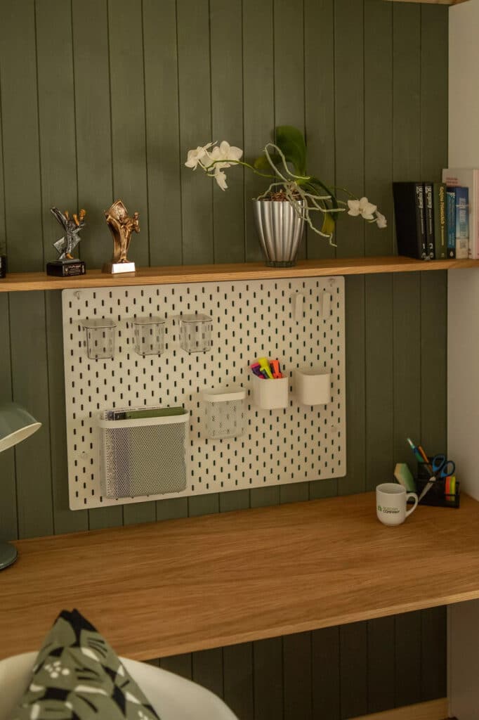 Dedicated home office space with a wooden desk, a white pegboard organizer, and green accent walls.