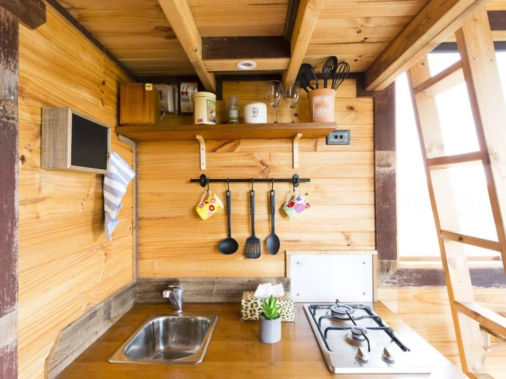 Compact kitchen design in a tiny house with wooden cabinetry, stainless steel sink, and gas cooktop.