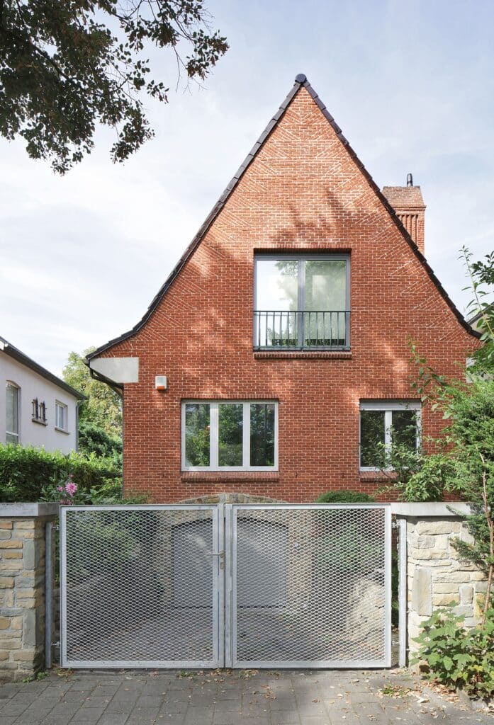 Close-up of the red brick facade featuring symmetrical windows with grey frames and a traditional gabled roof.