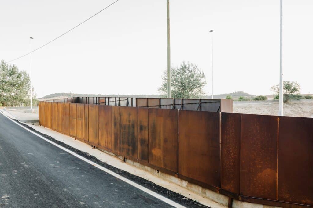 A side view of the continuous Corten steel panels lining the road and protecting the historical trench area.