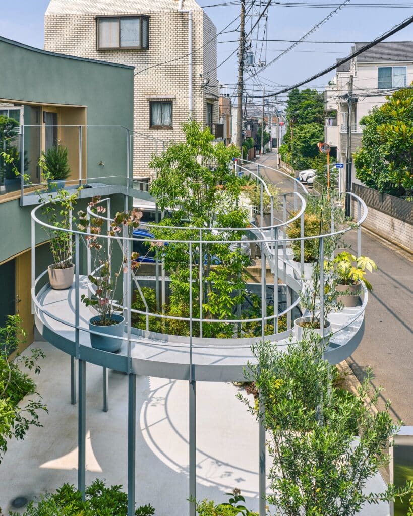 Close-up of a sculptural curved metal balcony with potted plants overlooking a narrow Tokyo street.