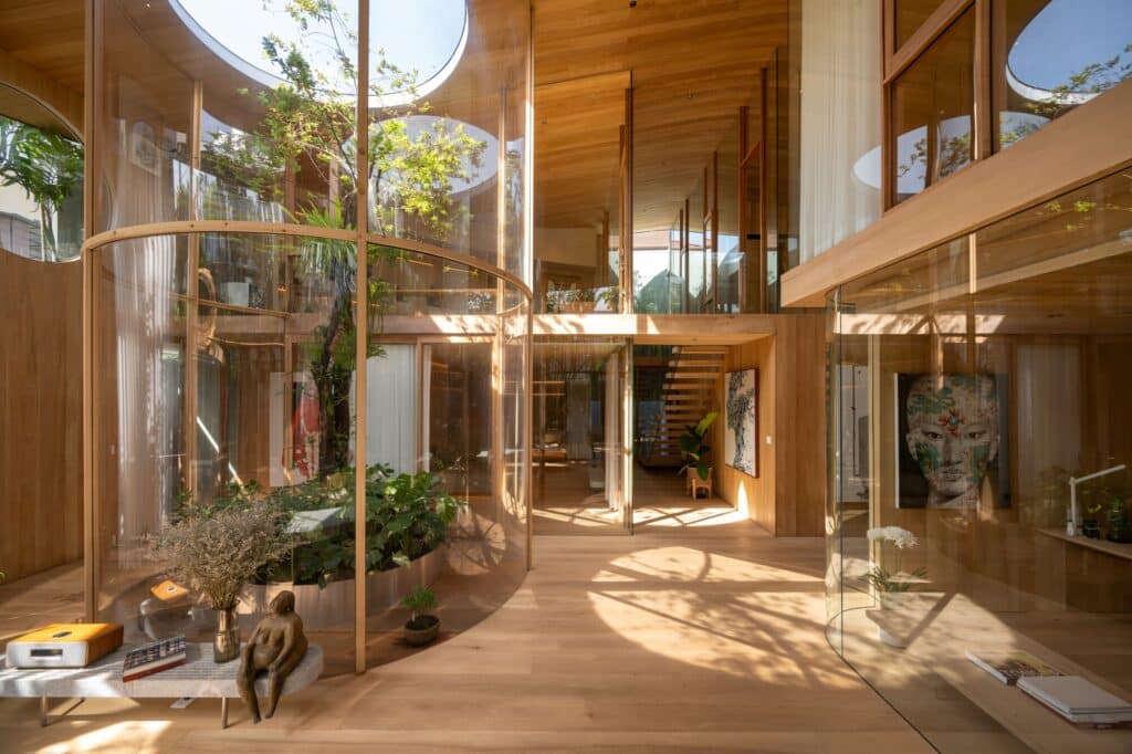 Interior view of Terrarium House showing a central glass-enclosed courtyard with lush trees and seamless wooden flooring.