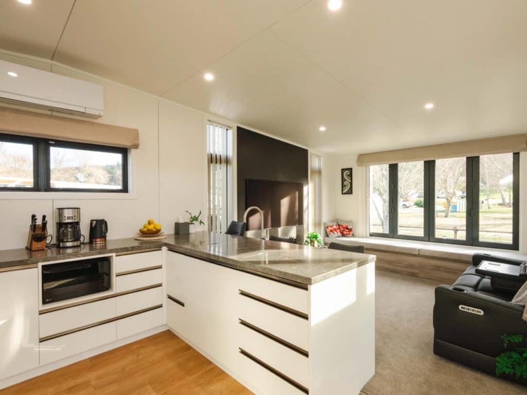 Bright open-plan kitchen and living area in a tiny house with white cabinetry and stone countertops.