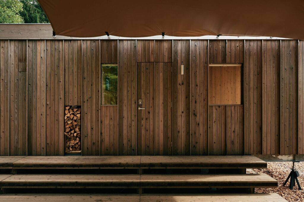 Frontal view of the Earthboat Cave entrance with wooden steps and a protective canopy, emphasizing the vertical lines of the timber.