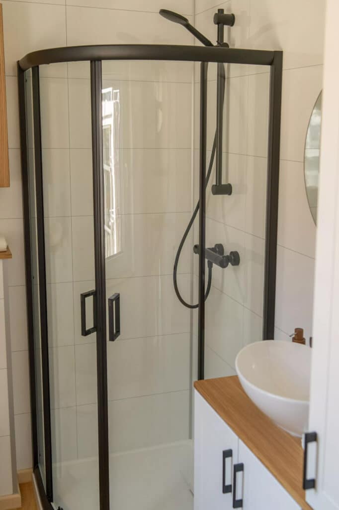 Contemporary bathroom with a curved glass shower enclosure, black fixtures, and a white vanity with wood accents.