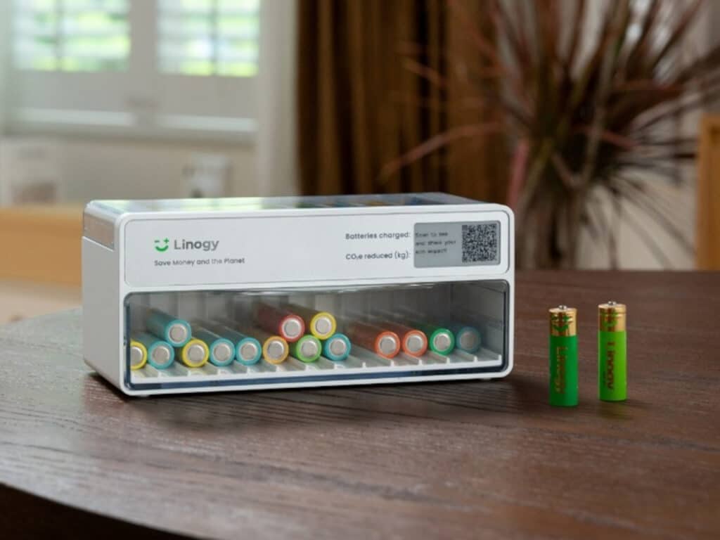 Front view of Linogy battery station on a dark wood table, showing organized rows of stored batteries through the transparent cover.
