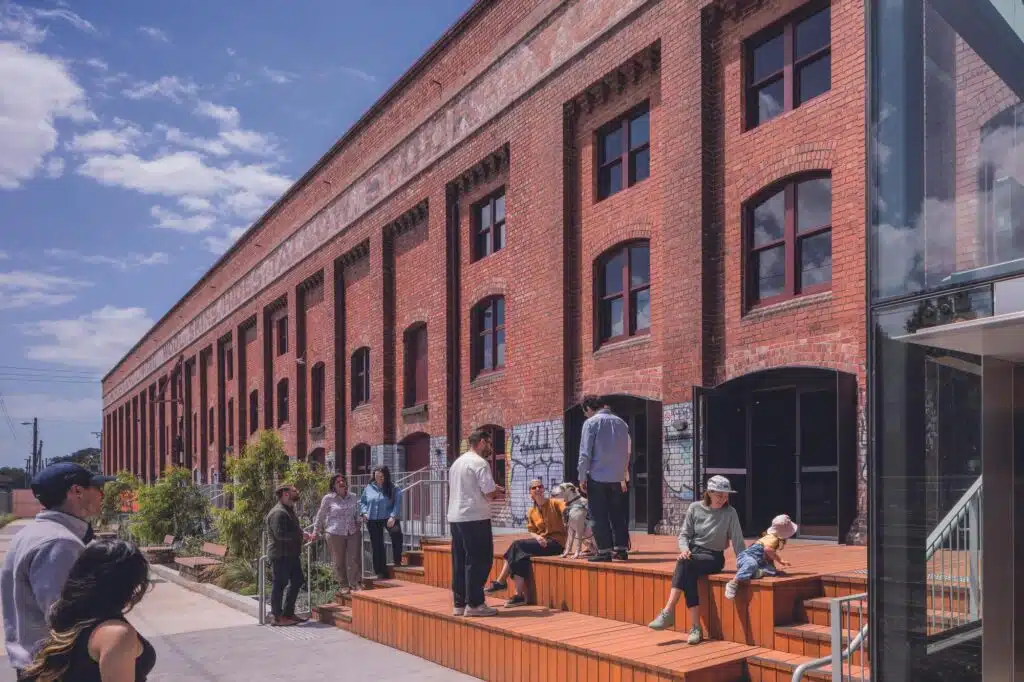People sitting on tiered timber seating outside a heritage red brick building, highlighting public realm activation at Younghusband.