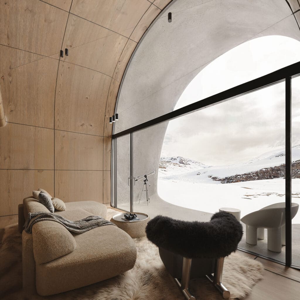 Interior of AltiHut showing a warm wood-lined living area with a large panoramic window overlooking snowy mountains.