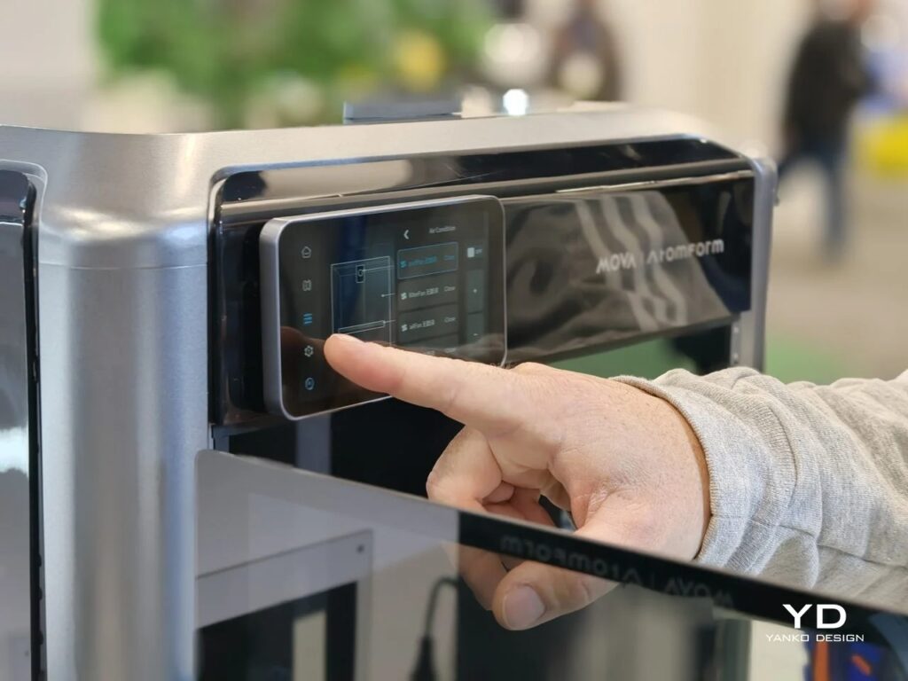 A user's finger touching the digital control panel of the AtomForm Palette 300 3D printer.