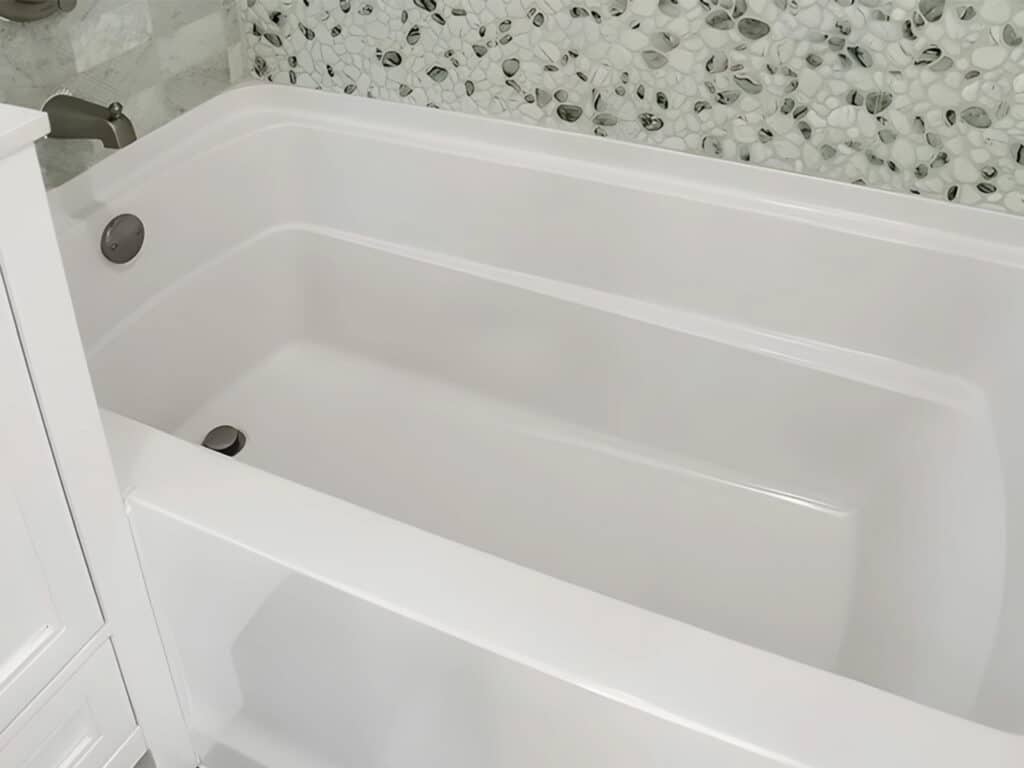 White modern bathtub in a tiny home with decorative marble-style mosaic wall tiles.