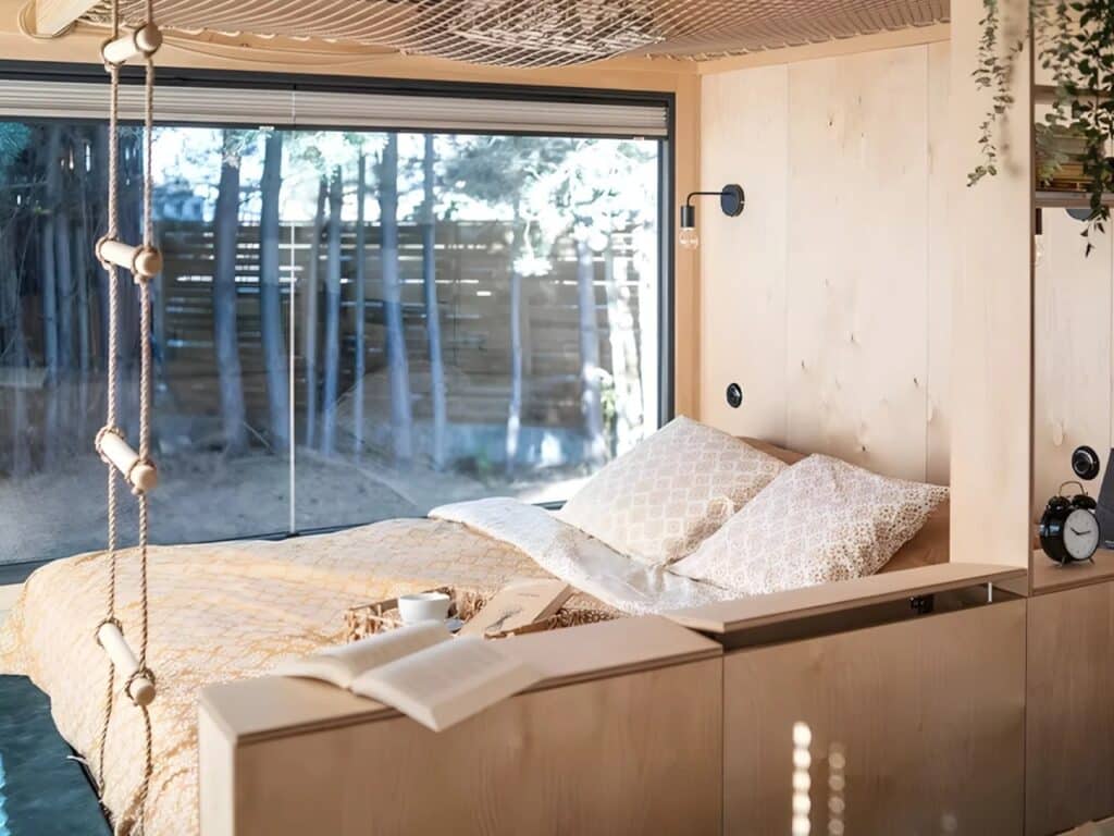Main bedroom area on the ground floor of Julia tiny home with a large bed and expansive views through glass walls.