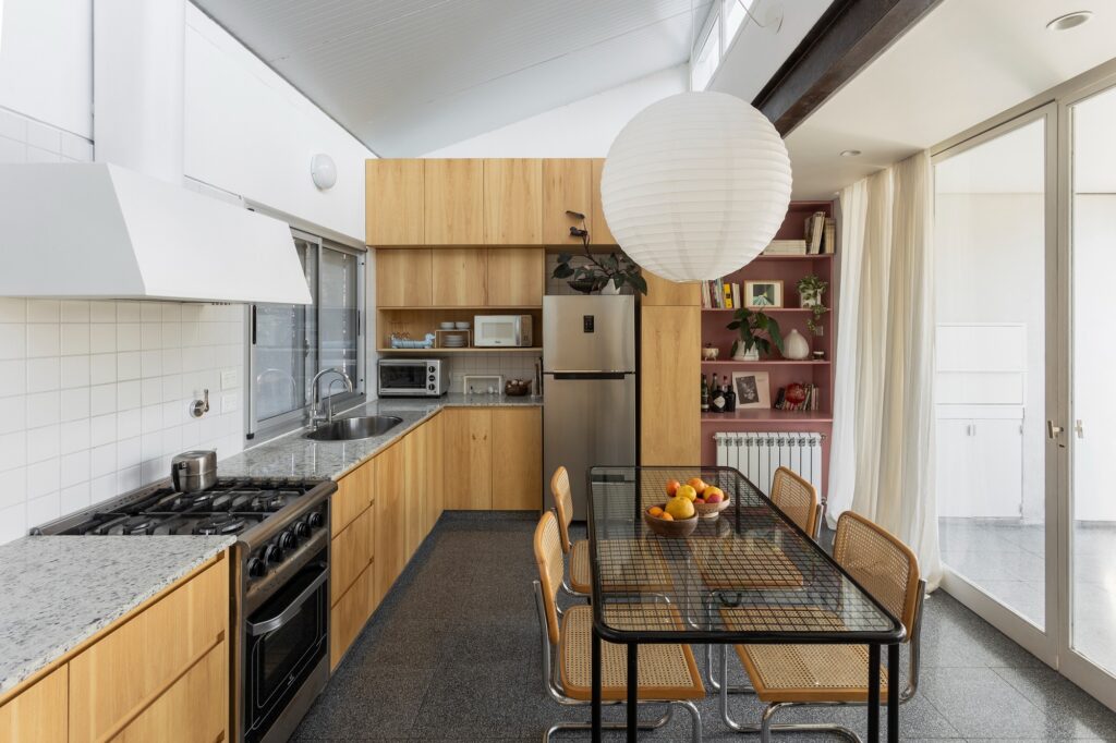 Modern kitchen detail with wooden cabinetry, granite countertops, and a dining table under a large paper globe pendant light.