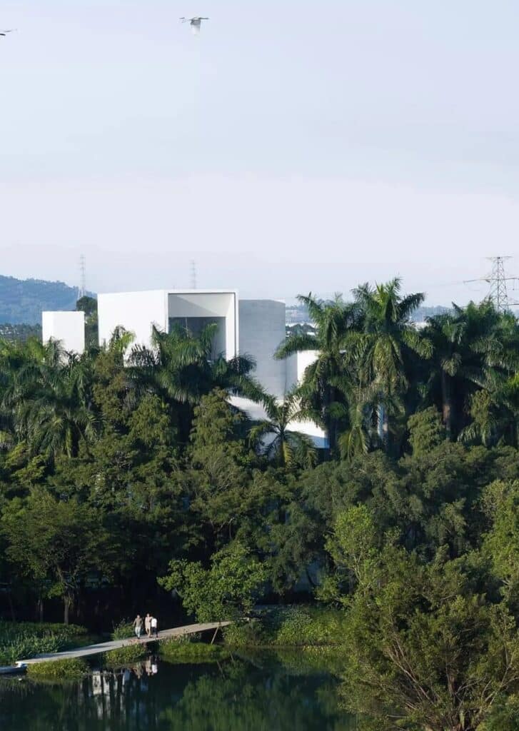 Visitors walking on a narrow bridge toward the Pearl River Delta Wetland Museum surrounded by tropical greenery.