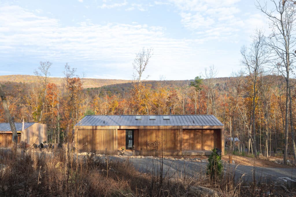Full frontal view of a Sera project villa showcasing the rhythmic wood screen and metal roof design in a natural mountain setting.