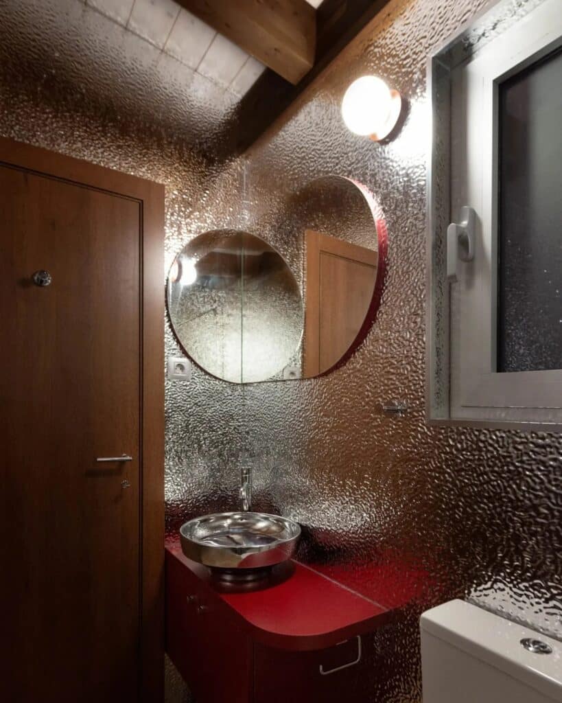 Bathroom interior of the Sava River Cabin with a metallic silver wall finish, a red vanity, and a round mirror.