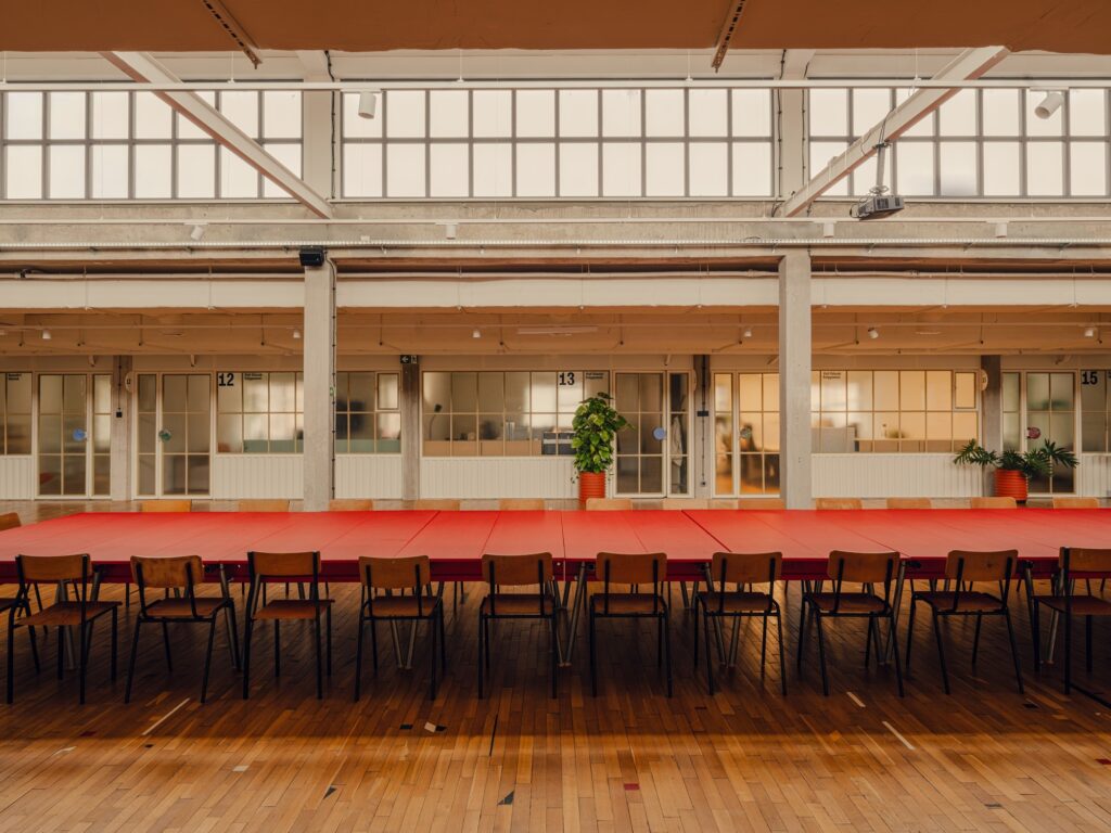 Long red communal work table in Grid Arthub's shared workspace with industrial windows in the background.
