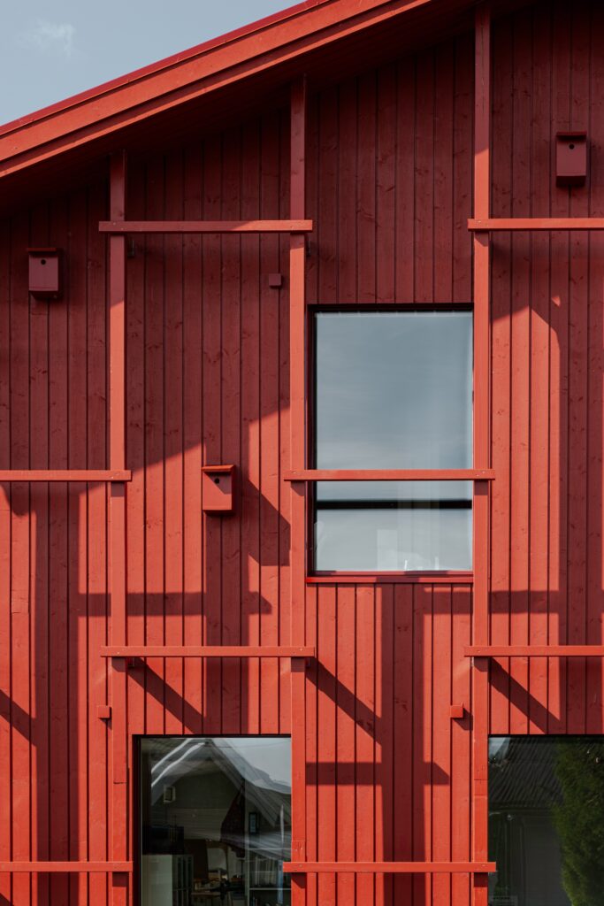 Close-up of the vertical wooden cladding and decorative trellis structure with small birdhouses on the red facade of Alvim Kindergarten.