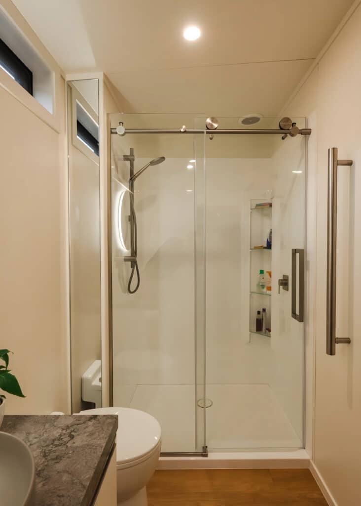Modern bathroom in a tiny home featuring a glass walk-in shower with sliding doors and a backlit mirror.