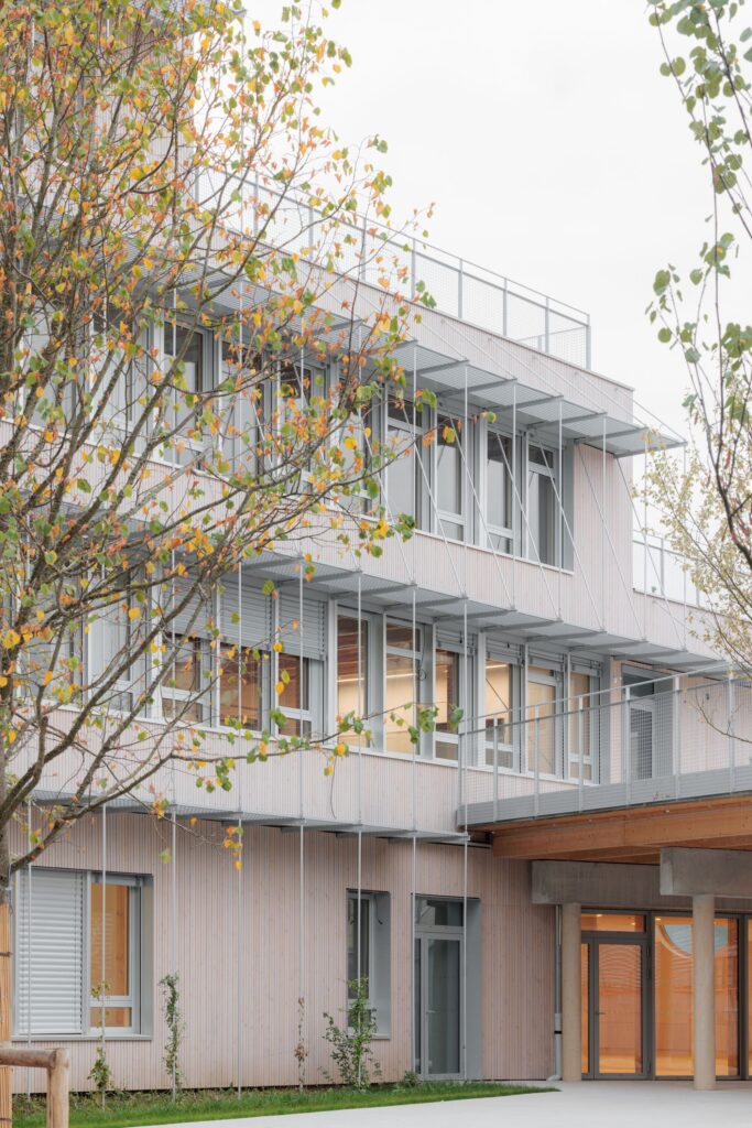 Exterior facade with metal sunshades over windows and a connecting walkway bridge.