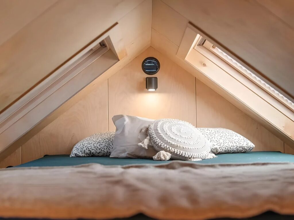 Upper loft sleeping area in Julia tiny home with a double bed, pitched roof, and dual skylight windows.
