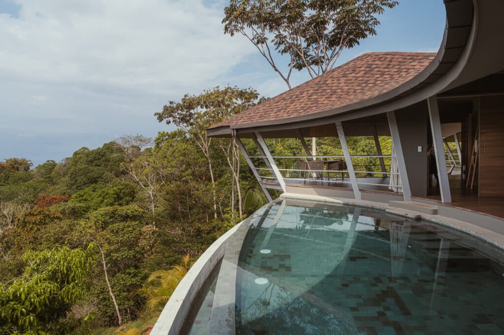 Infinity pool at Ojo de Nila house reflecting the sky and surrounding forest, extending toward the horizon.