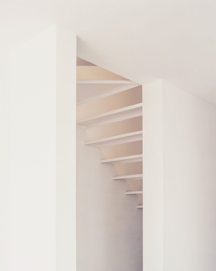 Minimalist white interior staircase with sharp architectural shadows.