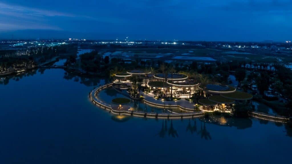 Night view of Lotus Club with warm lighting reflecting on the lake surface.