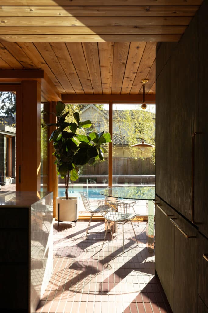 Interior dining area with a glass table and brick flooring, featuring floor-to-ceiling windows overlooking the swimming pool.