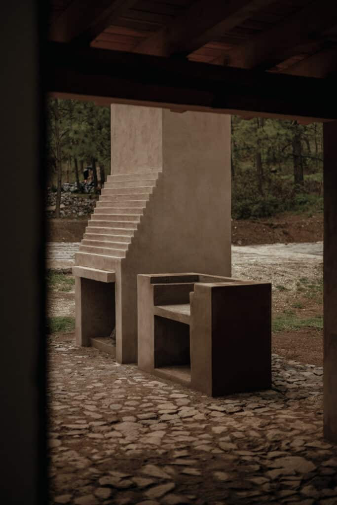 Close-up of a minimalist concrete outdoor stove and chimney structure on a stone floor.