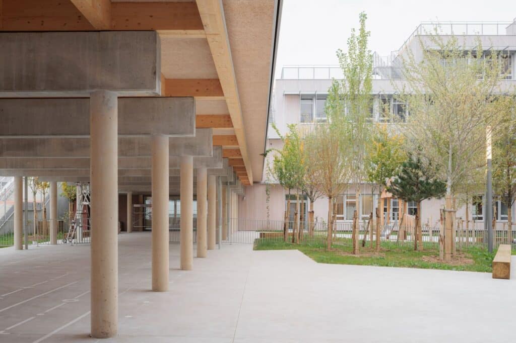 Covered outdoor play area with concrete columns and views of the landscaped school courtyard.