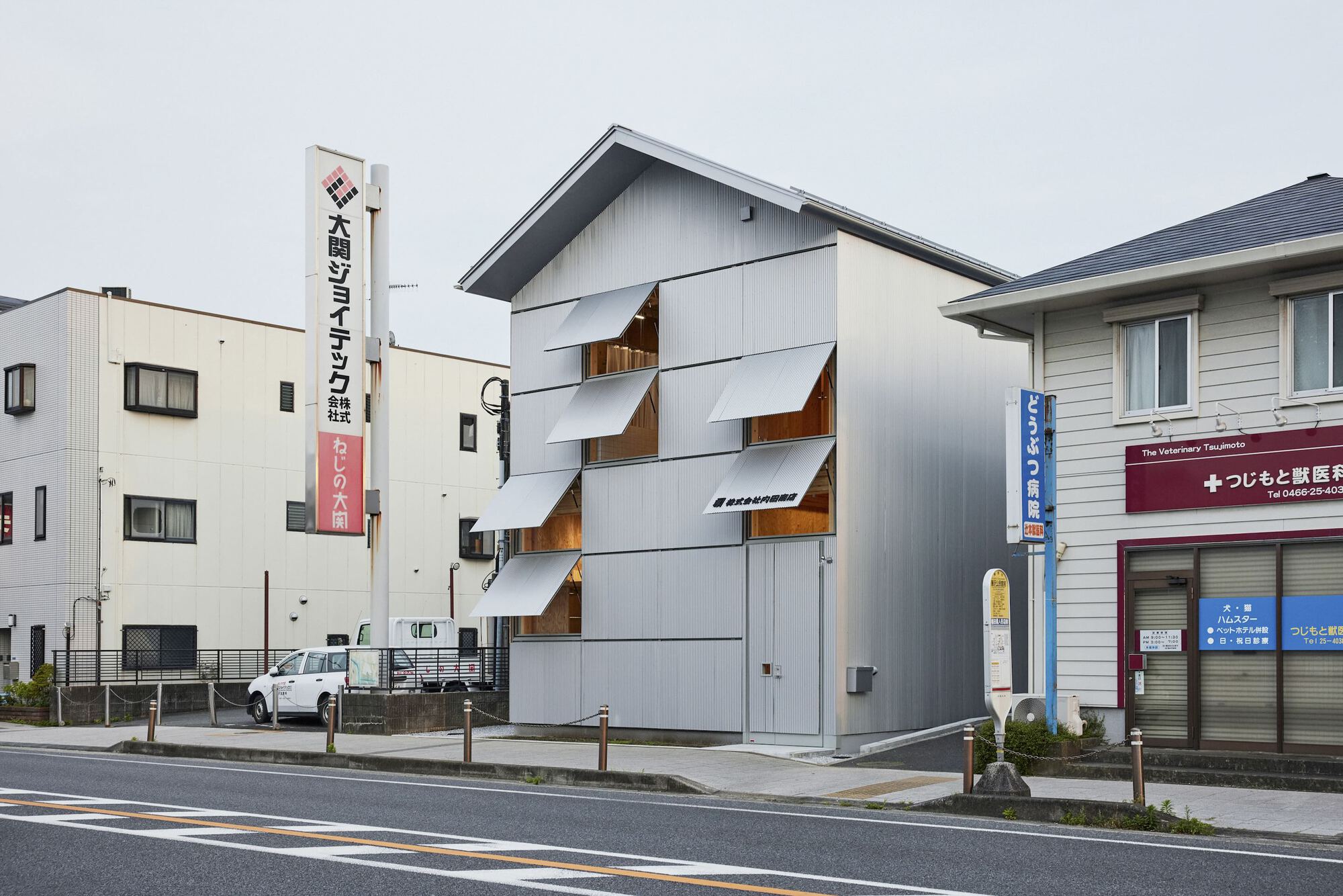 Street view of the Uchida Shoten building with some silver shutters partially open at different angles, creating a dynamic facade.