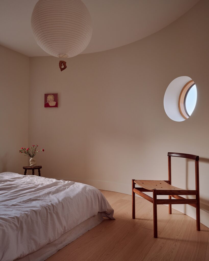 Minimalist bedroom in Runda House with a curved wall, circular window, and soft natural lighting.