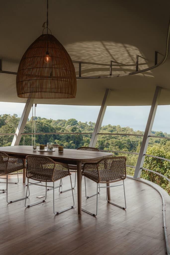 Dining area of Ojo de Nila house with a large wicker pendant light and panoramic views of the forest.