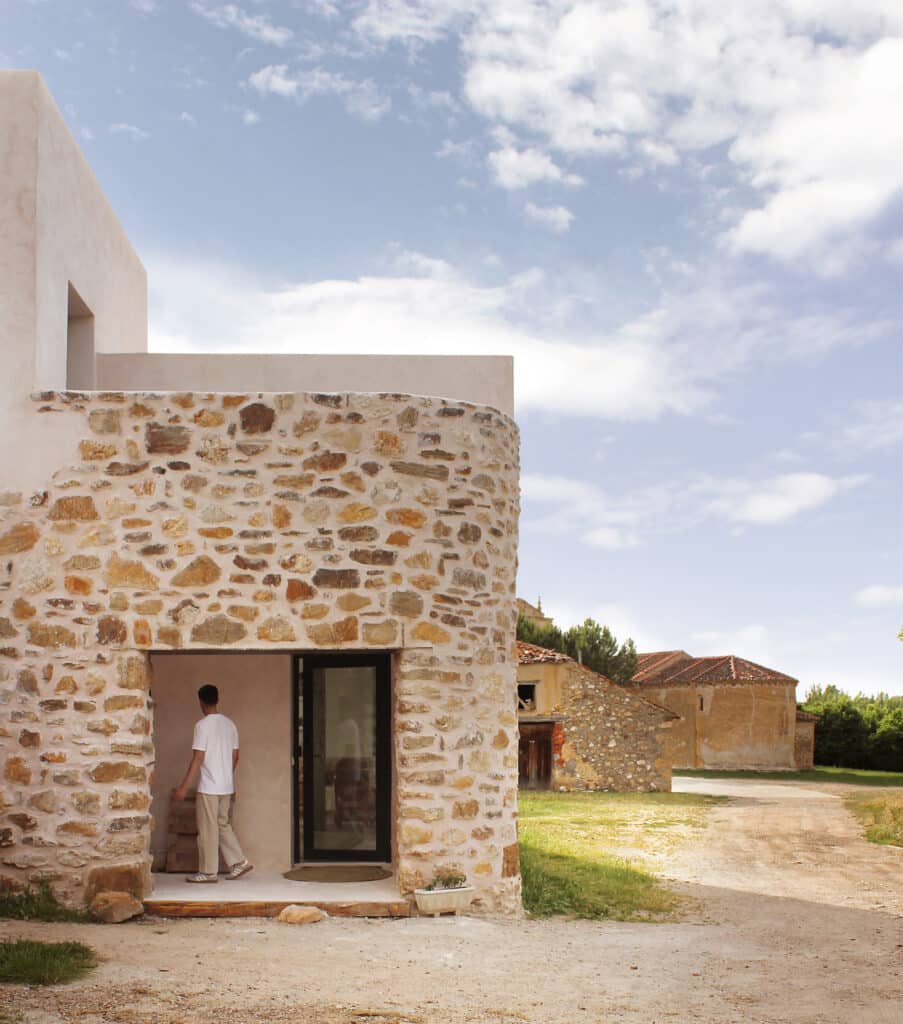Entrance of the rural house featuring a curved stone wall and a view of the nearby Romanesque church bell tower.