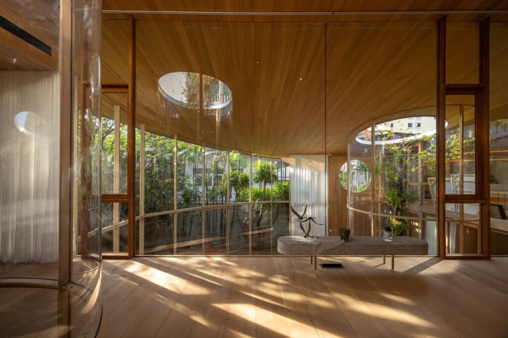 Upper floor workspace in Terrarium House featuring curved glass walls and a circular roof opening that reveals the sky and treetops.