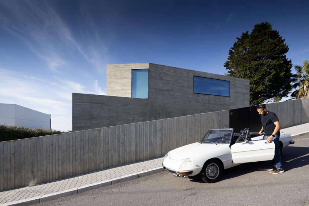A man standing by a classic white car in front of the contemporary exposed concrete walls of JA House in Portugal.