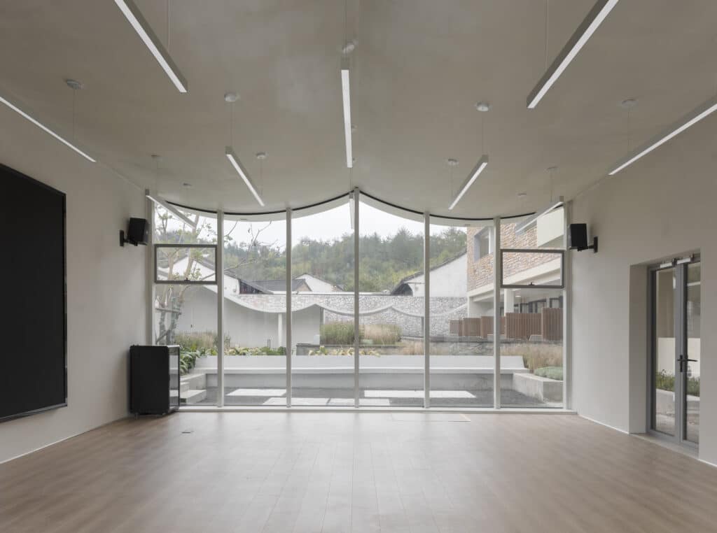 Interior of a multi-functional hall with floor-to-ceiling glass windows overlooking a sunken courtyard.