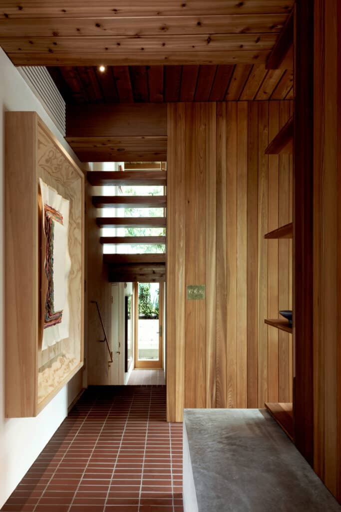 Interior hallway featuring a wooden staircase, fabric-wrapped gypsum walls for art display, and red brick tile flooring.